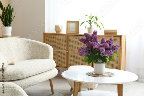 Stylish interior of living room with bouquet of lilacs branches on coffee table near white sofa