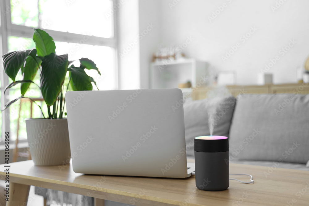 Fototapeta premium Air humidifier with laptop and plant on table in living room, closeup