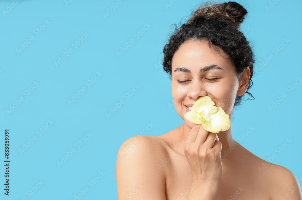 Beautiful young African-American woman with yellow orchid flower on blue background Beautiful young African-American woman with yellow orchid flower on blue background