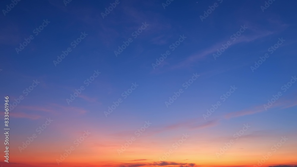 A beautiful sunrise with a clear sky transitioning from deep blue at the top to vibrant orange at the horizon. Light pink clouds are scattered across the sky, enhancing the tranquil scene.
