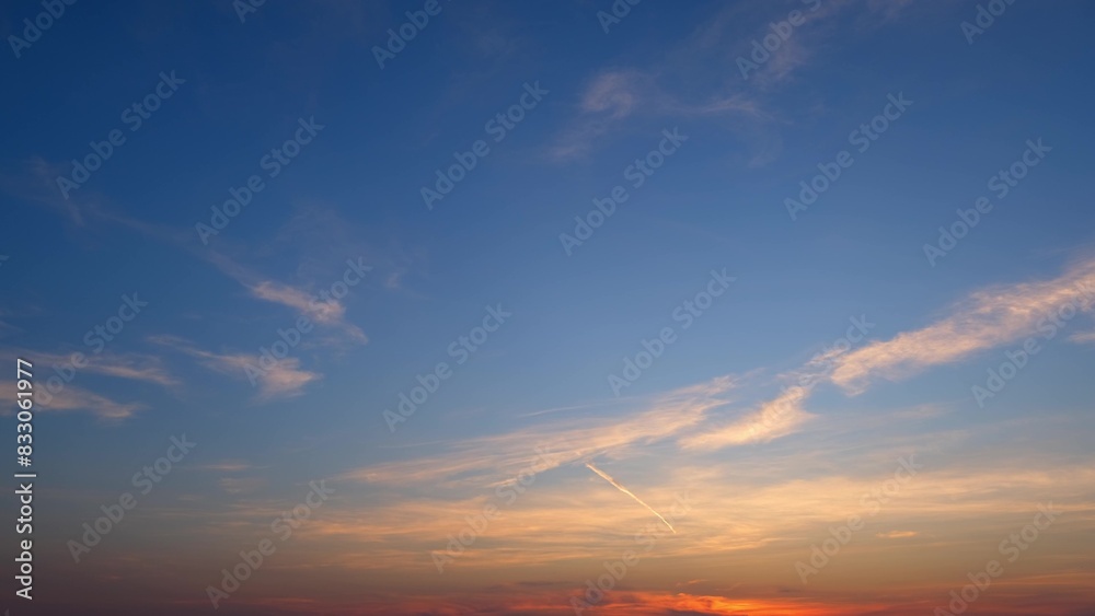 A serene sunrise with a sky that transitions from deep blue at the top to warm orange hues near the horizon. Wispy clouds are gently scattered, adding to the tranquil ambiance. 
