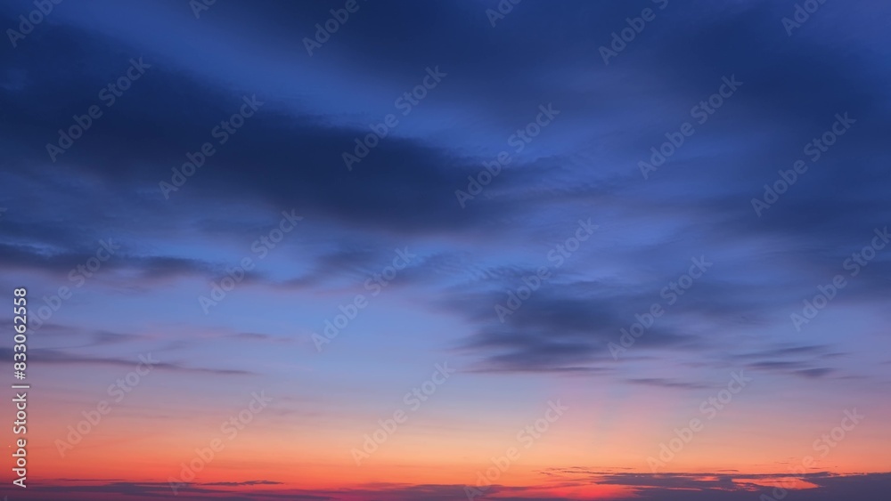 A stunning sunrise with deep blue clouds spread across the sky, gradually transitioning to a warm orange and pink hue near the horizon, creating a beautiful gradient. Sunrise sky background.
