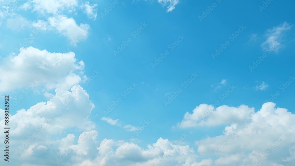 Obraz premium A beautiful blue sky filled with large, fluffy white clouds. The clouds are scattered across the sky, creating a sense of depth and dimension, enhancing the overall serene and calming atmosphere. 
