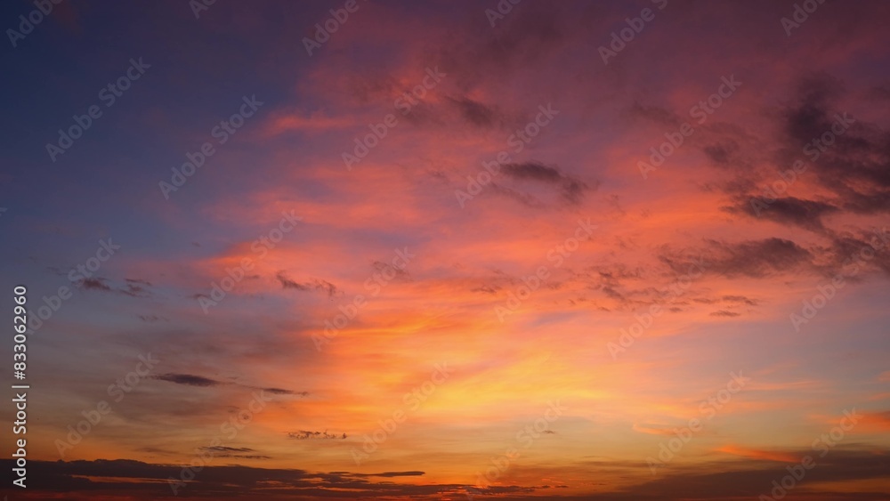 A beautiful sunrise with vibrant orange and pink hues illuminating the sky. The clouds are tinged with shades of purple and dark patches, creating a dramatic and serene scene. Sunrise sky background.
