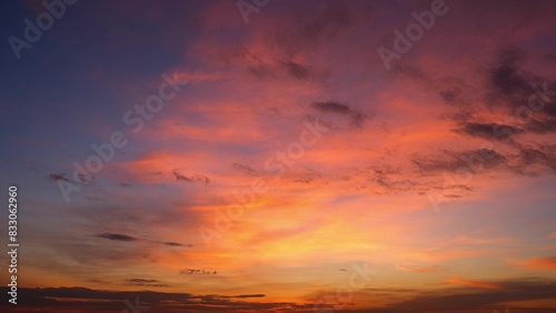A beautiful sunrise with vibrant orange and pink hues illuminating the sky. The clouds are tinged with shades of purple and dark patches  creating a dramatic and serene scene. Sunrise sky background. 