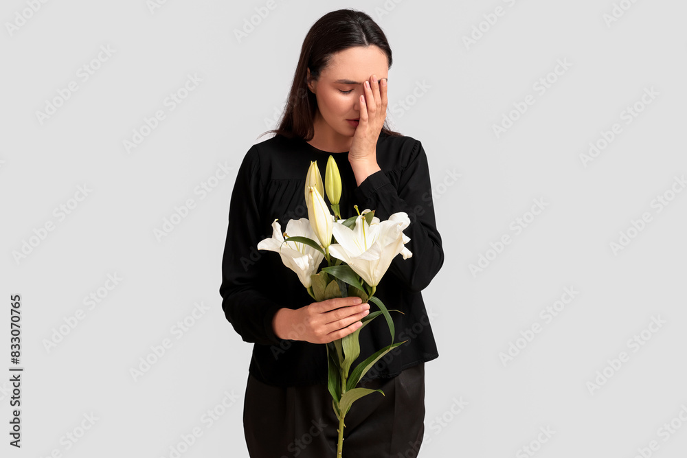 Young crying woman with funeral lily flowers on white background Young crying woman with funeral lily flowers on white background