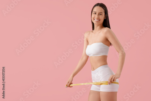 Beautiful young happy woman with measuring tape on pink background. Weight loss concept