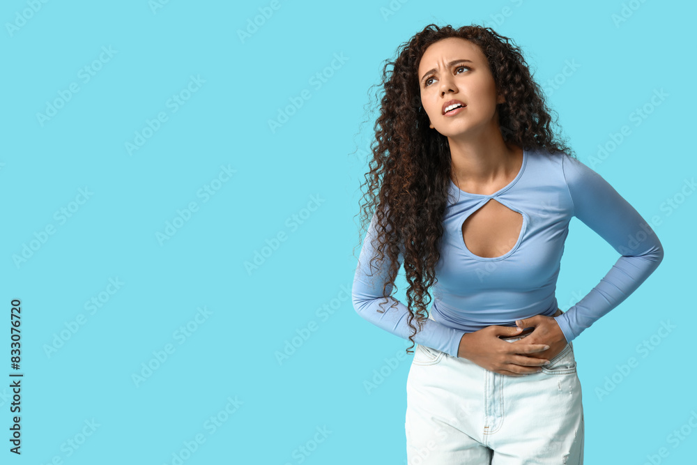 Young African-American woman with stomach ache on blue background Young African-American woman with stomach ache on blue background
