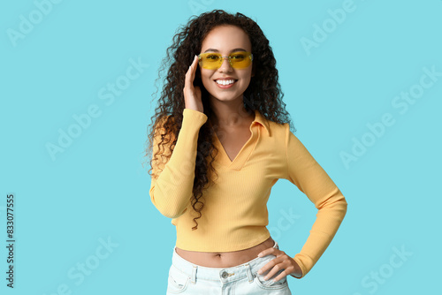 Happy young African-American woman in sunglasses on blue background © Pixel-Shot