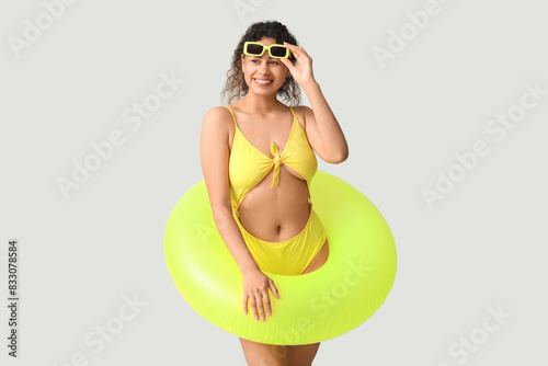 Beautiful young African-American woman in stylish yellow swimsuit with inflatable ring on grey background © Pixel-Shot
