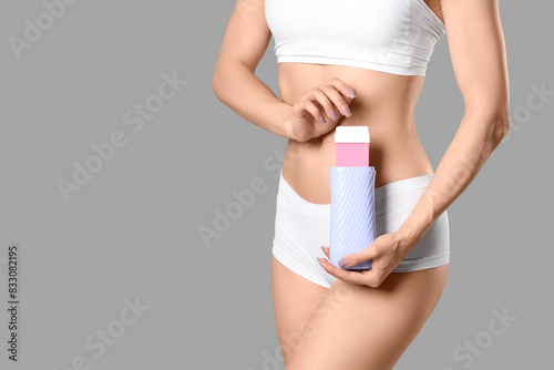 Beautiful young woman with liposoluble wax cartridge on grey background, closeup. Depilation concept photo