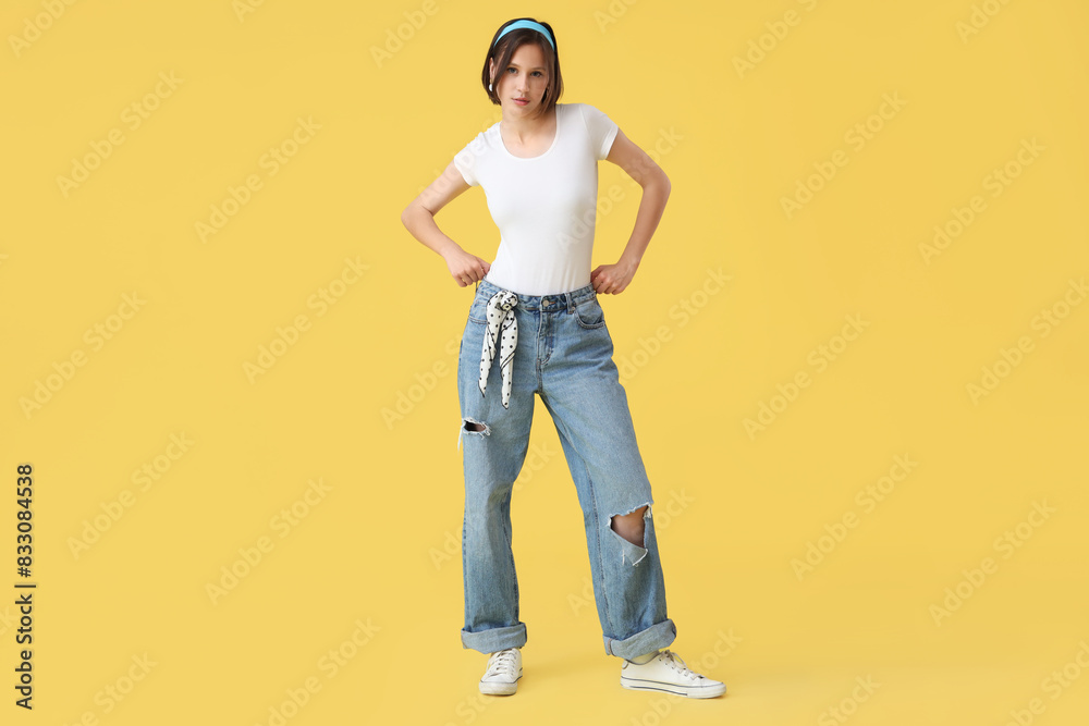 Beautiful young woman in stylish jeans on yellow background Beautiful young woman in stylish jeans on yellow background