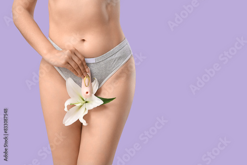 Beautiful young woman in underwear with vibrator from sex shop and lily flower on purple background, closeup