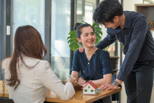 Real estate agent discussing contract with a couple, property model on desk, home buying consultation in modern office setting.