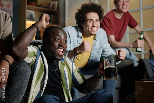 Young African American guy and his multi-ethnic friends having fun watching soccer game match on TV in evening