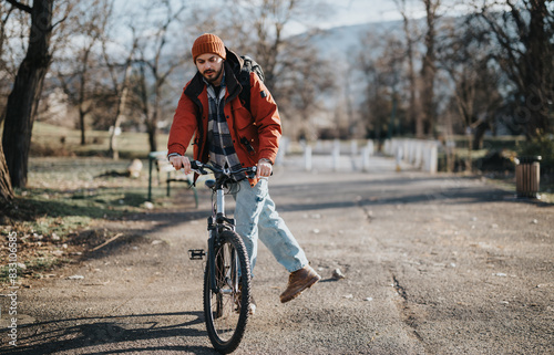 An active man in casual attire enjoys a leisurely bike ride in a serene park setting with autumn vibes.