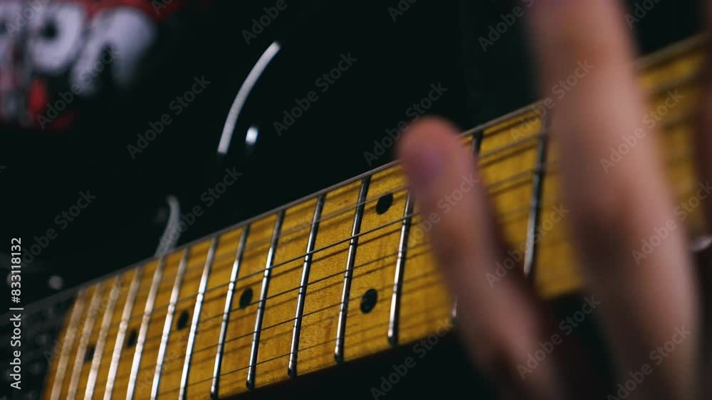 A close-up of the fingerboard of an electric guitar, a man's fingers strumming the strings. Slow motion of a guitarist playing. The man plays a hard metal riff