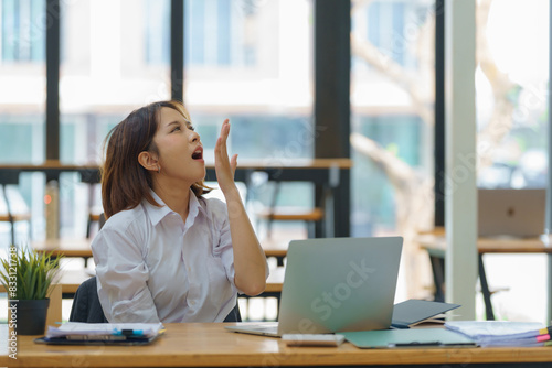Asian businesswoman yawning while working with a laptop computer.