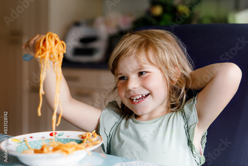 Obraz na płótnie Adorable toddler girl eat pasta spaghetti with tomato bolognese with minced meat. Happy preschool child eating fresh cooked healthy meal with noodles and vegetables at home, indoors. w salonie