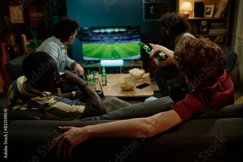 Fotografía Rear view of four young male friends spending evening indoors watching soccer ma