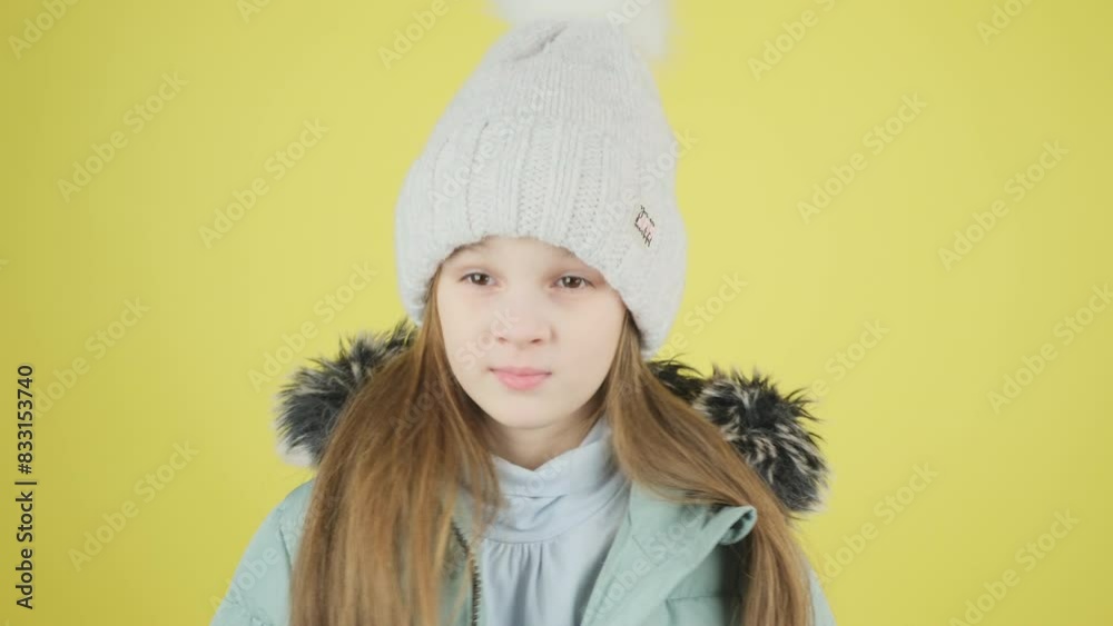 A beautiful little girl in a green down jacket and hat looks and smiles at the camera, blows a kiss on a yellow studio background. A beautiful little girl in a green down jacket and hat looks and smiles at the camera, blows a kiss on a yellow studio background.