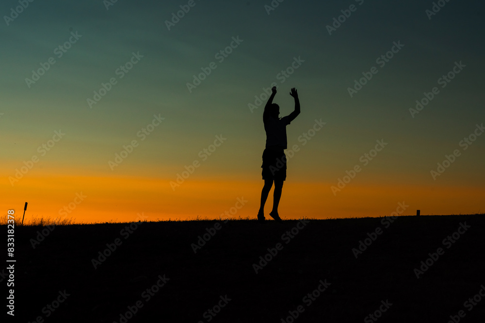 Silhouette of a person raising hands against a colorful sunset sky.