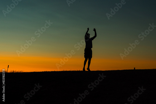 Silhouette of a person raising hands against a colorful sunset sky.