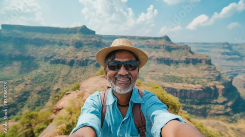 Man taking a selfie at the edge of a canyon, smiling, wearing a hat and sunglasses, on a sunny day © Darya Lavinskaya