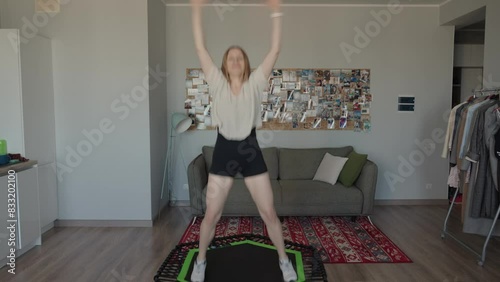 Energetic woman enjoying a fitness workout on a trampoline at home. She is jumping on the trampoline in a modern living room.