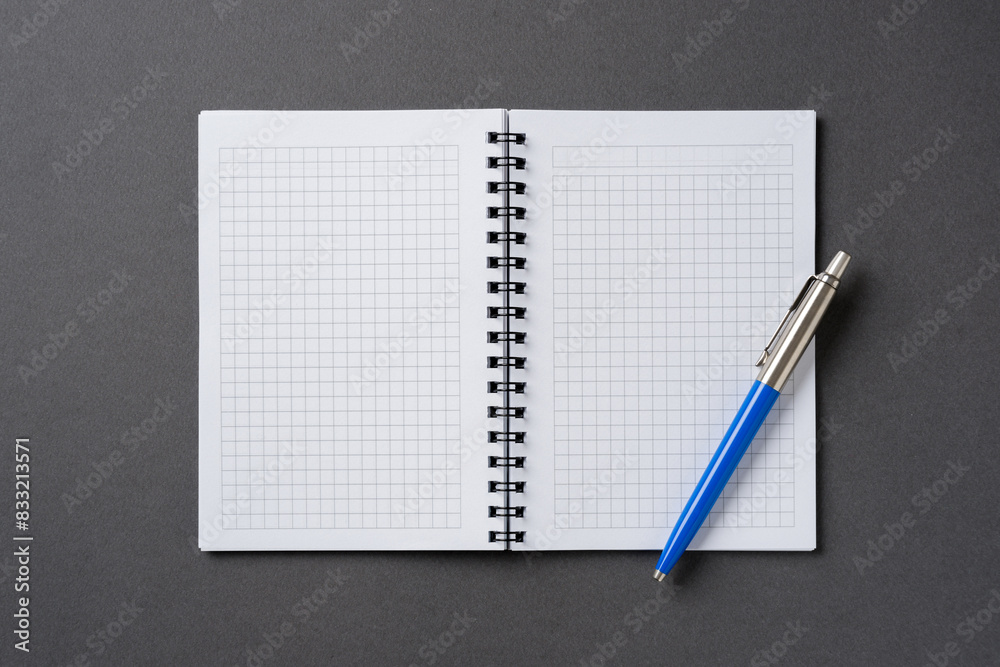 Checkered and spiral notebook on a dark gray table with a ballpoint pen next to it Checkered and spiral notebook on a dark gray table with a ballpoint pen next to it