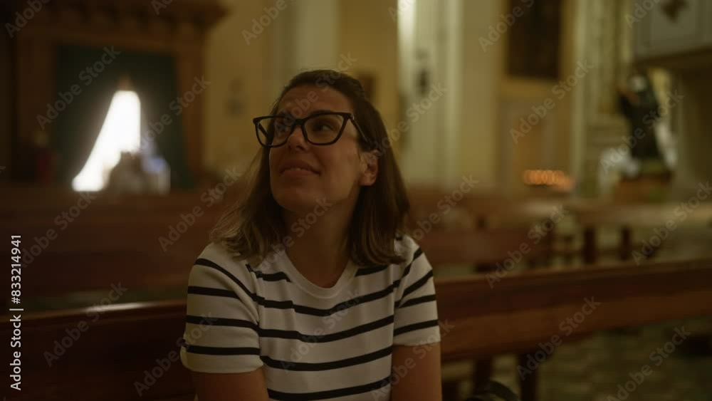 Young woman with glasses in striped shirt sits inside an italian christian church, looking up and admiring the interior with a peaceful expression. Young woman with glasses in striped shirt sits inside an italian christian church, looking up and admiring the interior with a peaceful expression.