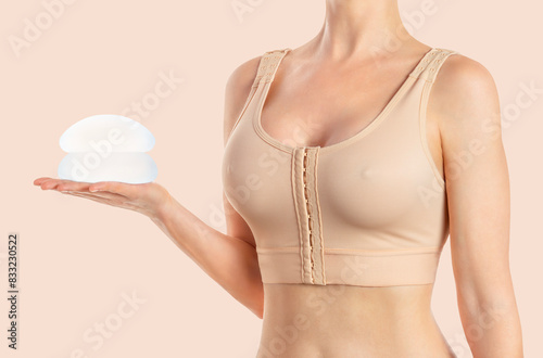 Woman holds round implants wearing compressing bra on beige background.