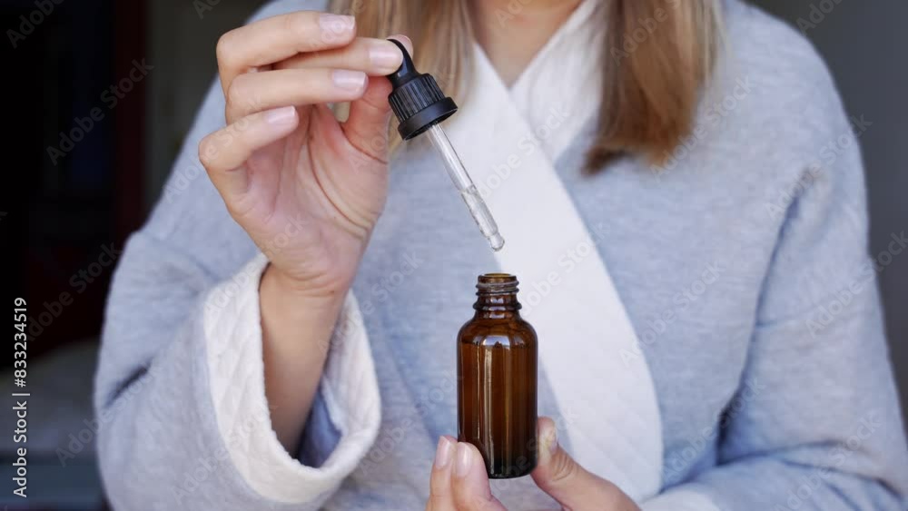 Hands of a young woman with a drop of serum or hyaluronic acid from a pipette. Young woman is applying moisturizing serum on her skin.