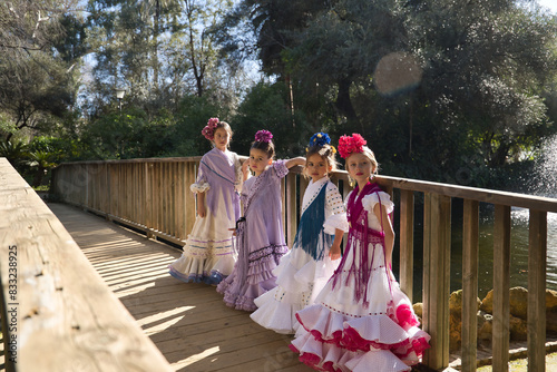 Four girls dancing flamenco, posing looking at the camera, in typical flamenco dress, on a wooden bridge. Concept dance, flamenco, typical Spanish, Seville, Spain.