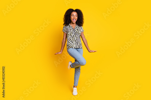 Portrait of glamour young cute american girl curly hair in zebra print shirt and jeans dancing energetic isolated on yellow color background © deagreez