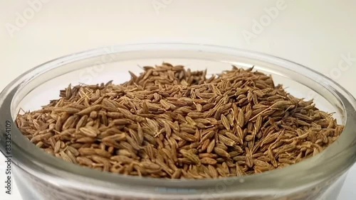 Cumin seeds drops in a glass bowl on white background, a glass bowl full of cumin seeds in the center, rotating, micro shot, herbs and spices. photo