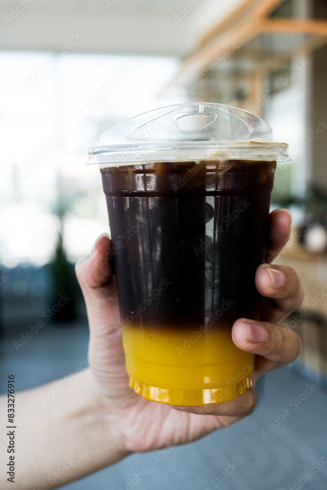 A glass of iced americano black coffee mix with orange juice showing a layer in man hand A glass of iced americano black coffee mix with orange juice showing a layer in man hand