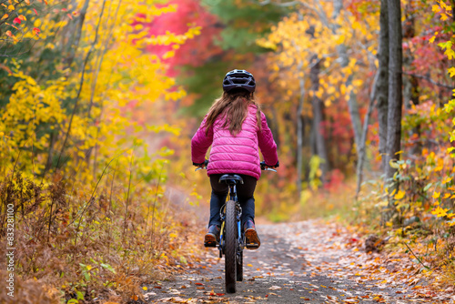 Young girl enjoying a peaceful autumn cycling adventure through the vibrant and colorful forest trail. Surrounded by the stunning fall foliage and scenic nature