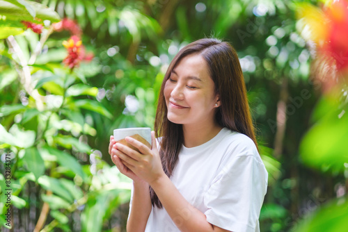 Portrait image of a young woman with closed eyes holding coffee cup and relaxing in the garden