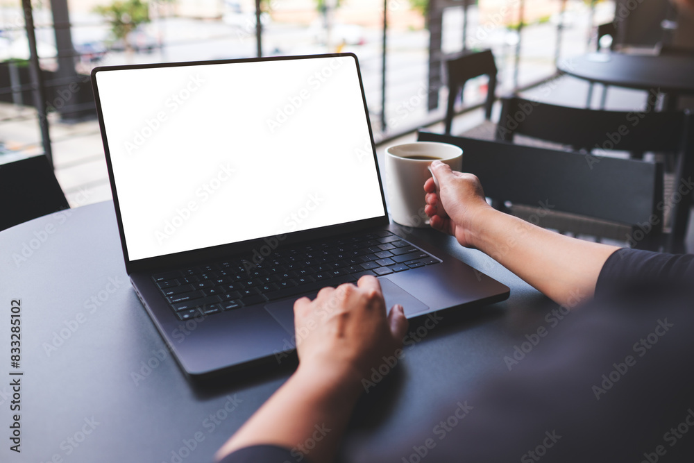 Mockup image of a woman working on laptop computer with blank white desktop screen while drinking coffee in cafe