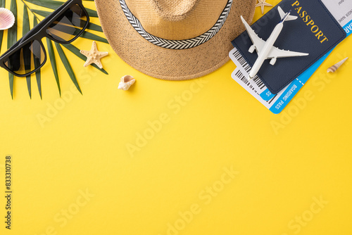 Flat lay image of summer travel essentials including straw hat, sunglasses, passport, and shells on a vibrant yellow background photo