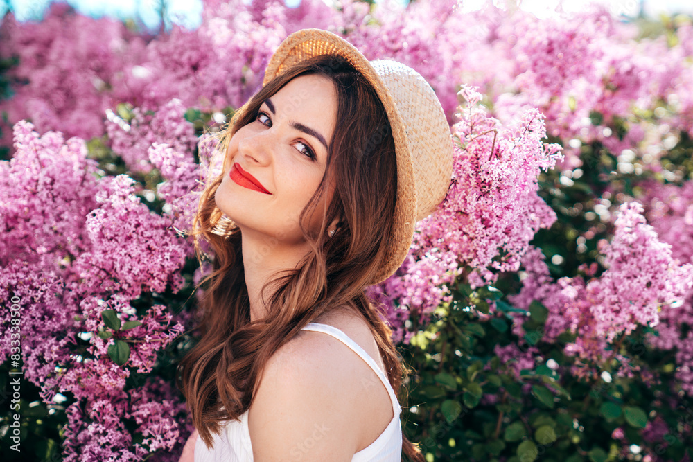 Young beautiful smiling woman in trendy summer clothes. Sexy carefree model posing in the street. Positive model near blooming flower lilac bush beaming. Summertime, pink colours. Red lips, straw hat Young beautiful smiling woman in trendy summer clothes. Sexy carefree model posing in the street. Positive model near blooming flower lilac bush beaming. Summertime, pink colours. Red lips, straw hat