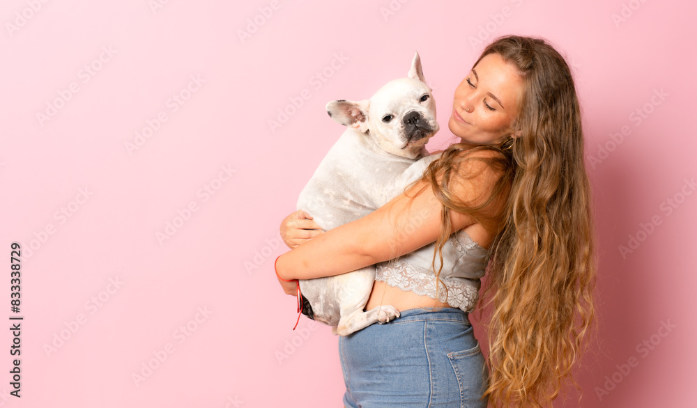 Happy young woman playing with french bulldog on pink background. Happy young woman playing with french bulldog on pink background.