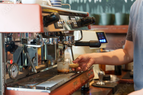 Close-up on hands of barista crafting espresso with professional machine  rich coffee brew flows into glass cup  symbolizes skilled craftsmanship  passion for coffee artistry.