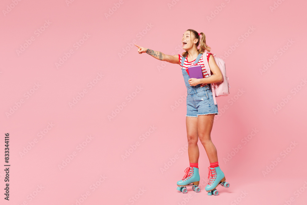Young girl student wear casual clothes backpack bag rollers rollerblading hold books point aside on area isolated on plain pink background Summer sport leisure, high school university college concept Young girl student wear casual clothes backpack bag rollers rollerblading hold books point aside on area isolated on plain pink background Summer sport leisure, high school university college concept