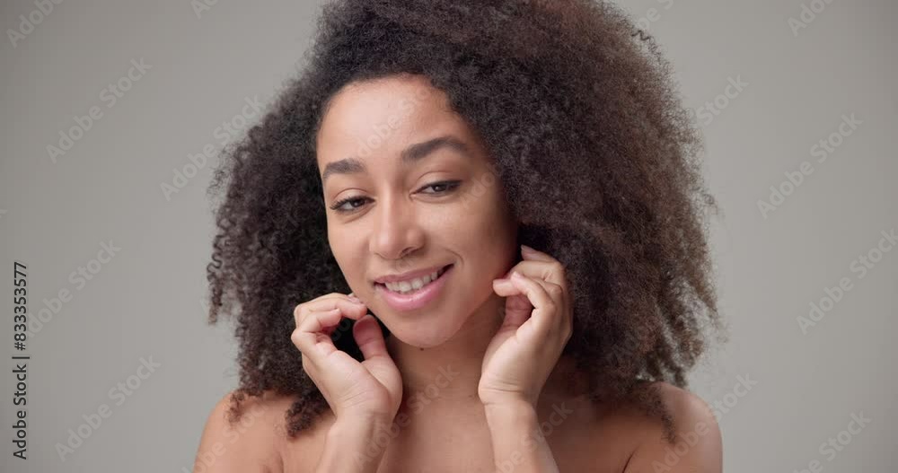 Beauty and healthcare concept - beautiful African American woman with curly afro hairstyle and clean, healthy skin touching face with hand, doing facial massage, posing and looking at camera