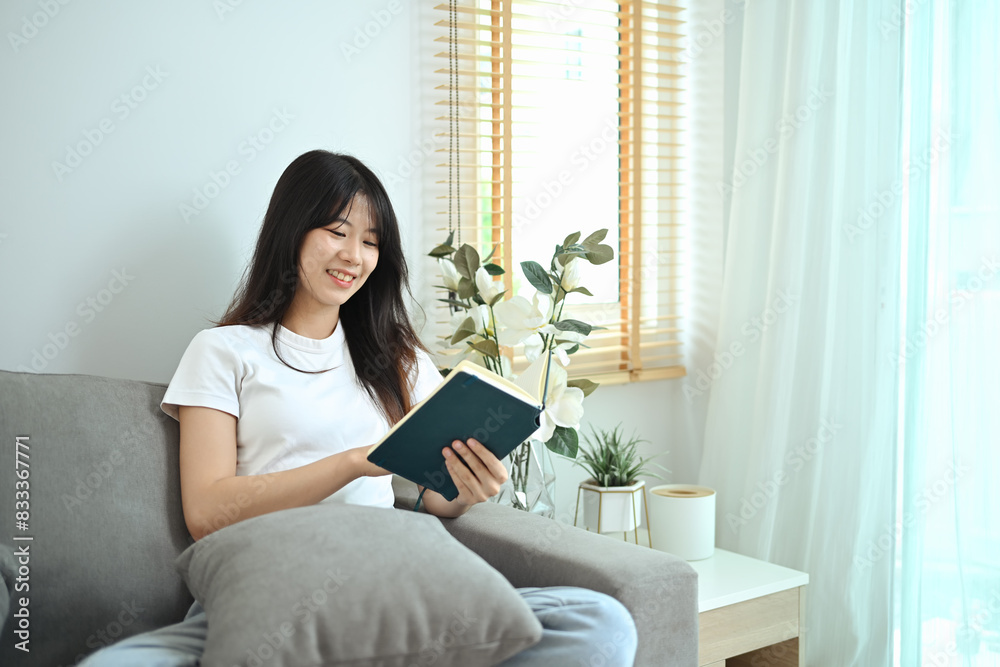 Happy young woman wearing casual clothes relaxing in her living room and reading book Happy young woman wearing casual clothes relaxing in her living room and reading book