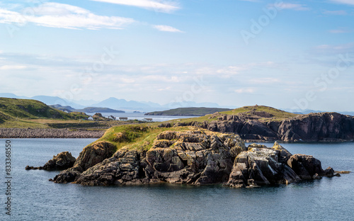 Obraz na płótnie The rocky coastline and blue water of Camas Eilean Ghlais with distant views of Reiff on a coastal walk in the Scottish Highlands on a sunny summers day in the UK. w salonie