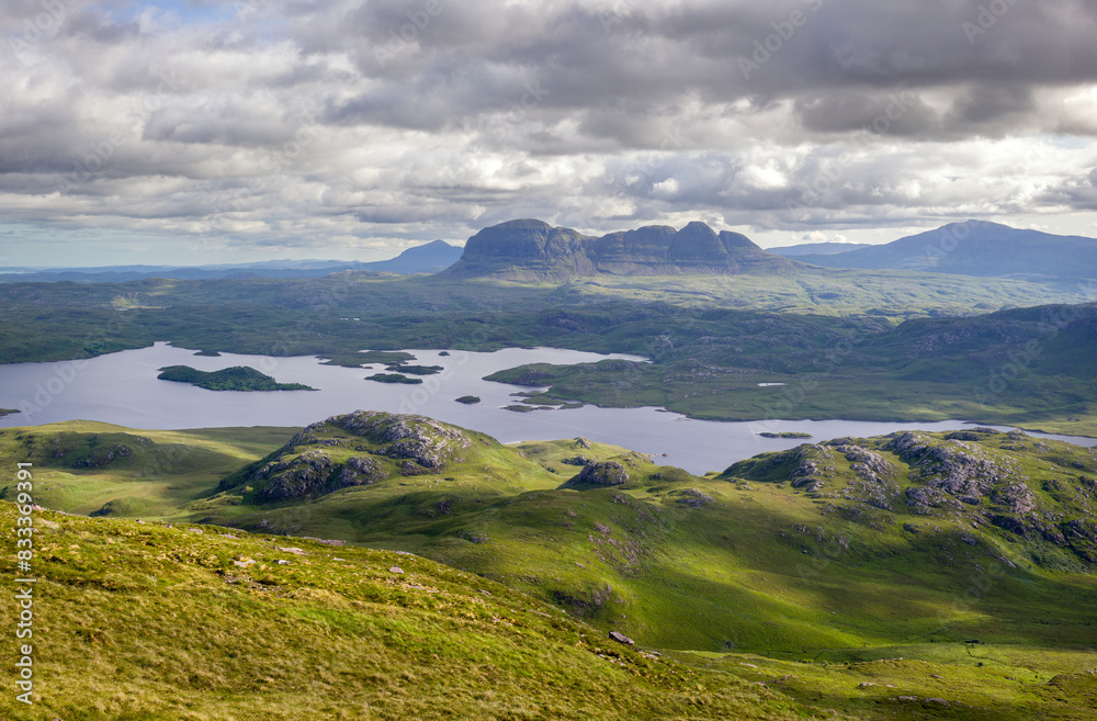 Views of the summits of Suilven, Caisteal Liath with Loch Sionasgaig below from the summit of Stac Pollaidh in the Scottish Highlands on a sunny summers day with dramatic clouds in the UK