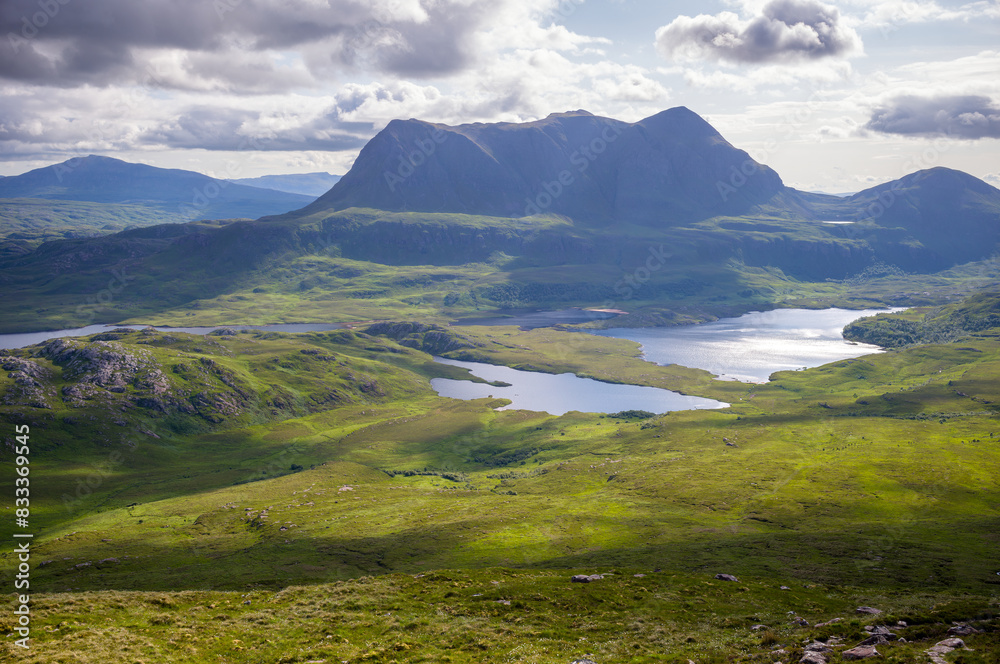 Views of the summits of Cul Mor and An Laogh with Loch an Doire Dhuibh below from the summit of Stac Pollaidh in the Scottish Highlands on a sunny summers day with dramatic clouds in the UK
